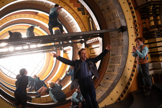 People climbing inside a large circular wooden structure with bright light at the center