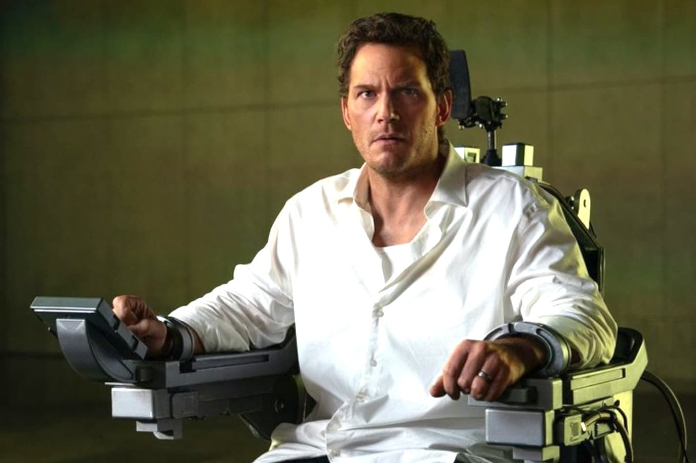 Chris Pratt sits strapped to a medical chair, looking concerned in a sterile room.