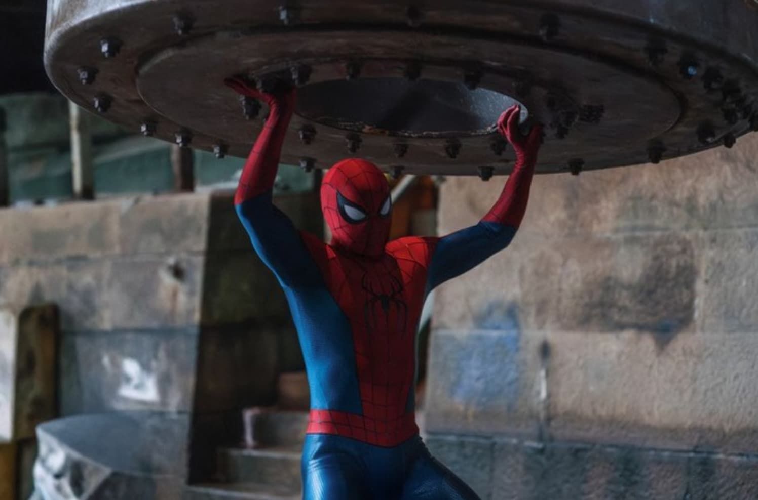 Spider-Man holding up a large metal platform in an industrial setting.