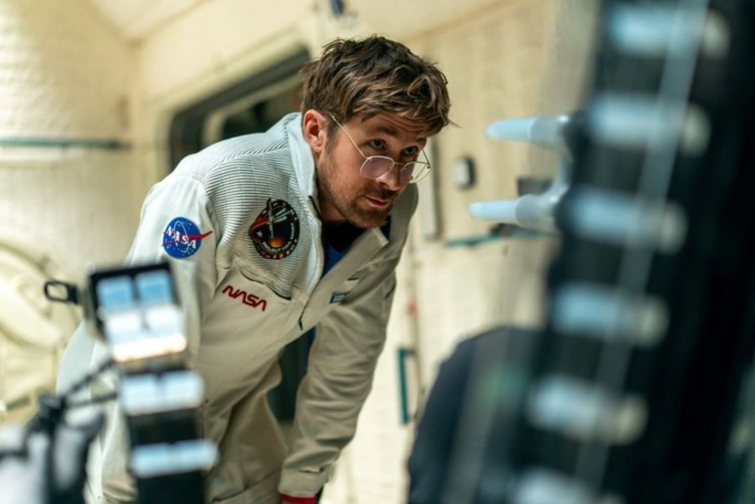 Astronaut in a white NASA suit leaning forward inside a spacecraft or station module