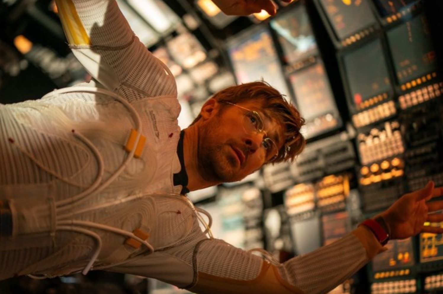 Man in white suit reaches through a futuristic control room with glowing panels.