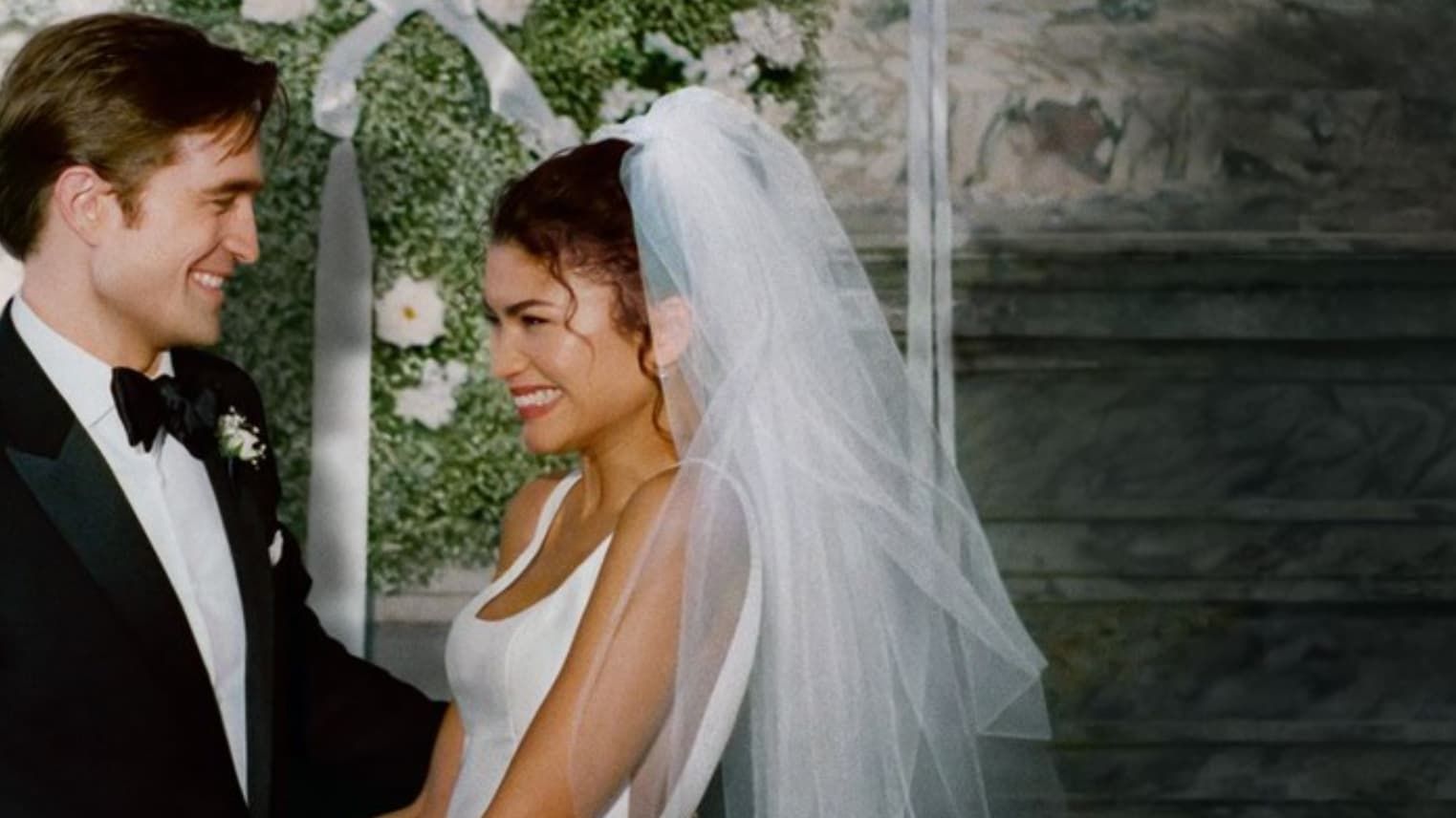 Bride and groom smiling at each other during a wedding ceremony, with white floral decorations behind them