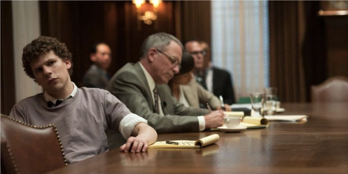 People seated at a conference table in a dim meeting room, with notebooks and glasses on the table