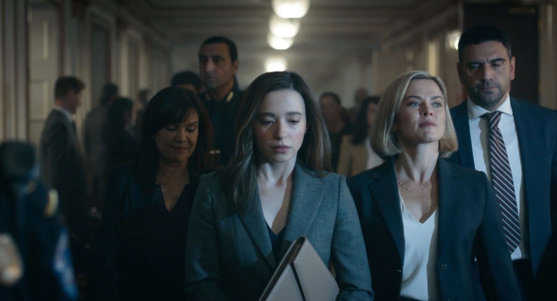 Business people walking down a hallway, with serious expressions and briefcases in a dim office setting