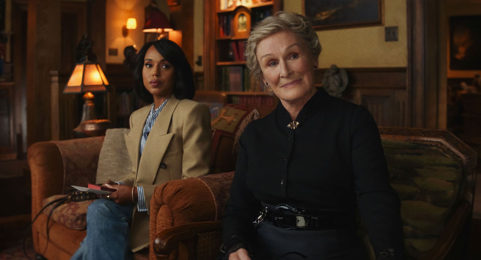Two people seated in a warmly lit living room, facing the camera with calm expressions.