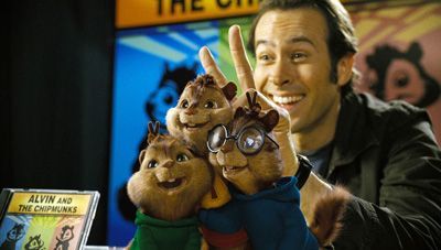 Man with chipmunk puppets, album cover in background. Man is smiling, chipmunks are puppets.