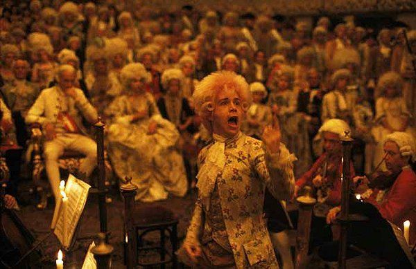 Man in floral coat singing to a crowd in a candlelit hall; 18th-century attire.