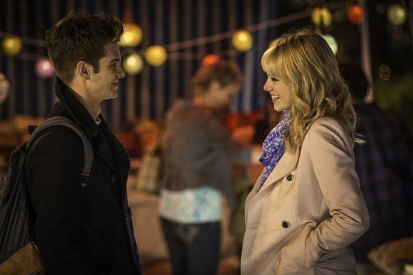 Man and woman smiling at each other outdoors, string lights in the background.