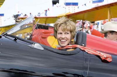 Woman smiling in a vintage airplane cockpit at an air show. Red scarf, blonde hair.