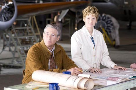 Richard Gere and a woman looking at blueprints in an airplane hangar.