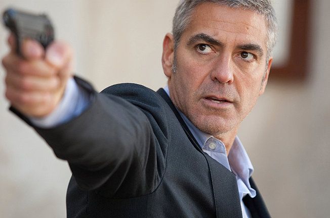 George Clooney aiming a handgun, looking focused, wearing a suit jacket.