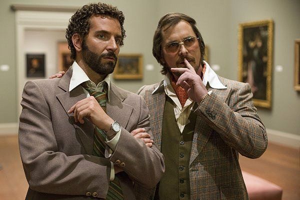 Two men in 70s attire pose in an art gallery.