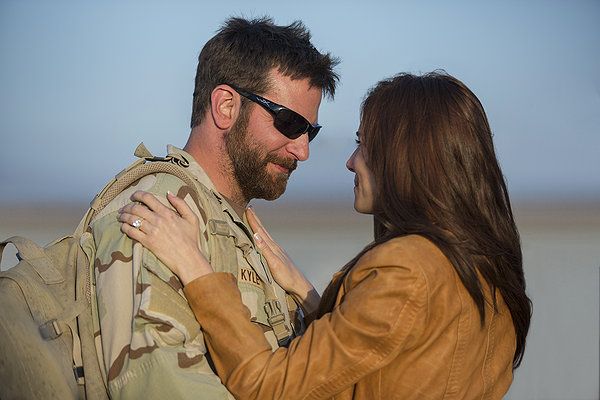Soldier in camo embraces a woman. They are outdoors, smiling.