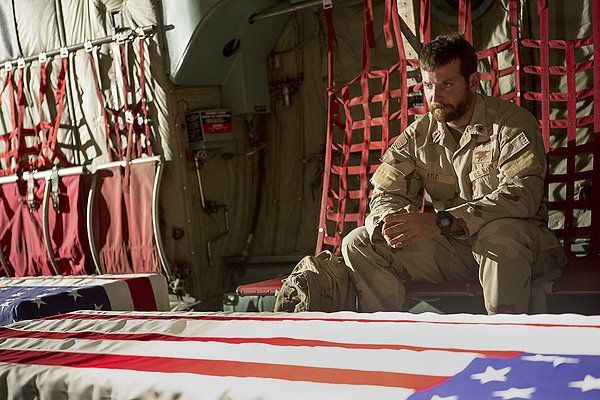 Soldier in uniform, seated, looks mournfully at flag-draped coffins