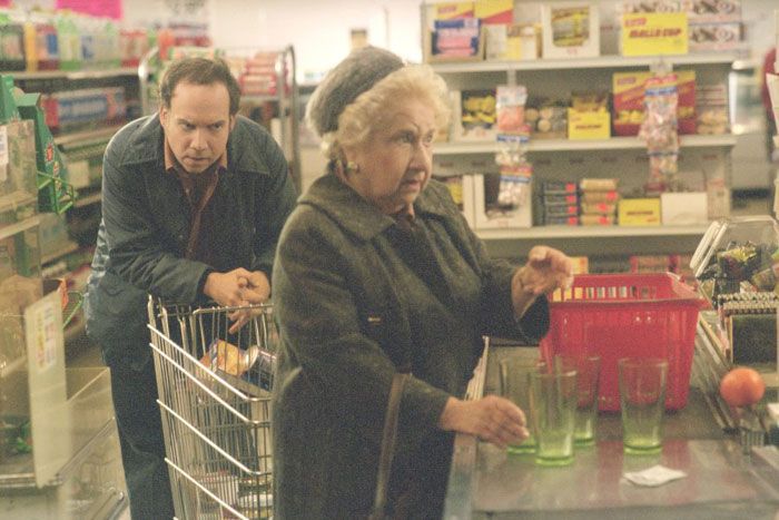 Man waits behind elderly woman at grocery store checkout; woman counts items on counter.