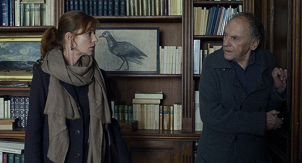 Woman in a scarf and man look on with concerned expressions in a library.