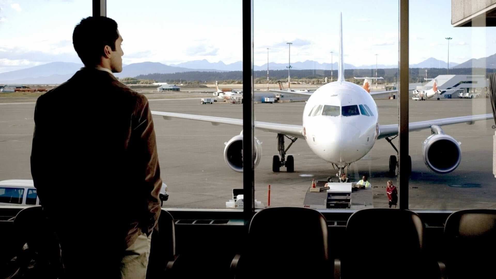 Traveler stands by airport window watching a plane on the tarmac.