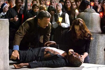 Man wounded, lying on ground; two people examine him. Group with candles in background.