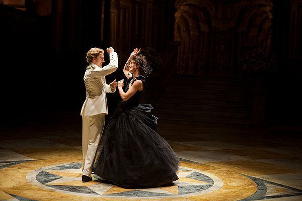 Two dancers in formal attire waltz in a dark setting.