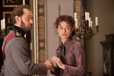 A man in uniform and a woman in a purple dress, looking at each other in a grand room.