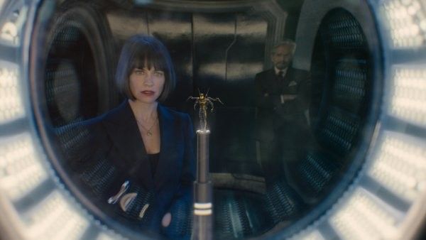 Woman in blue suit inside a circular pod with a figure in the background.