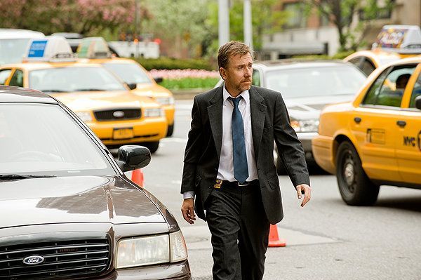 Man in suit walking on city street, cars and taxis in background.