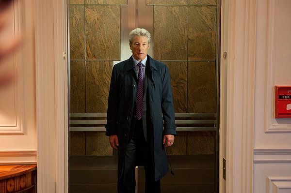Man in navy coat stands in elevator, looking forward, formal setting.