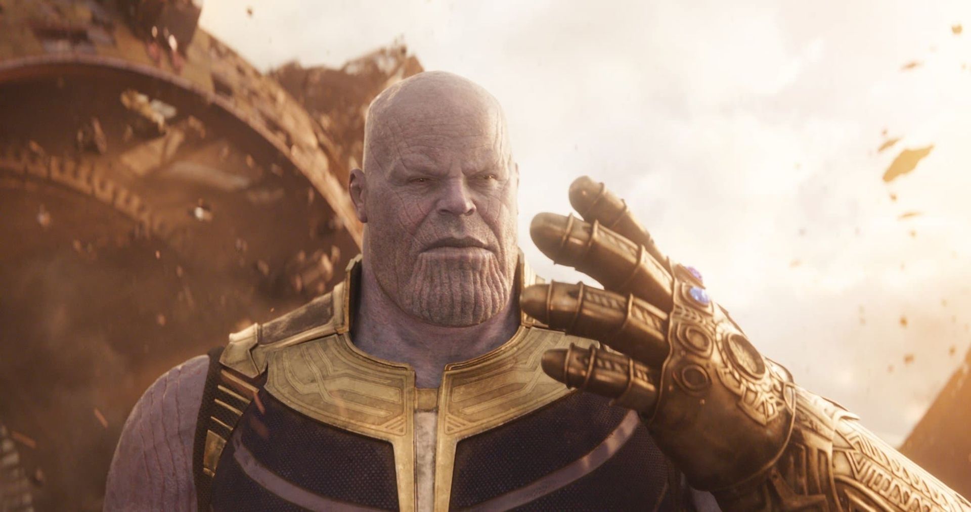 Thanos in gold armor raises his gauntlet amid a fiery battle scene