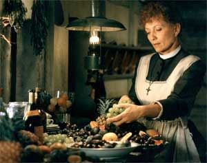 Woman in apron arranging fruit in a kitchen under a hanging lamp.