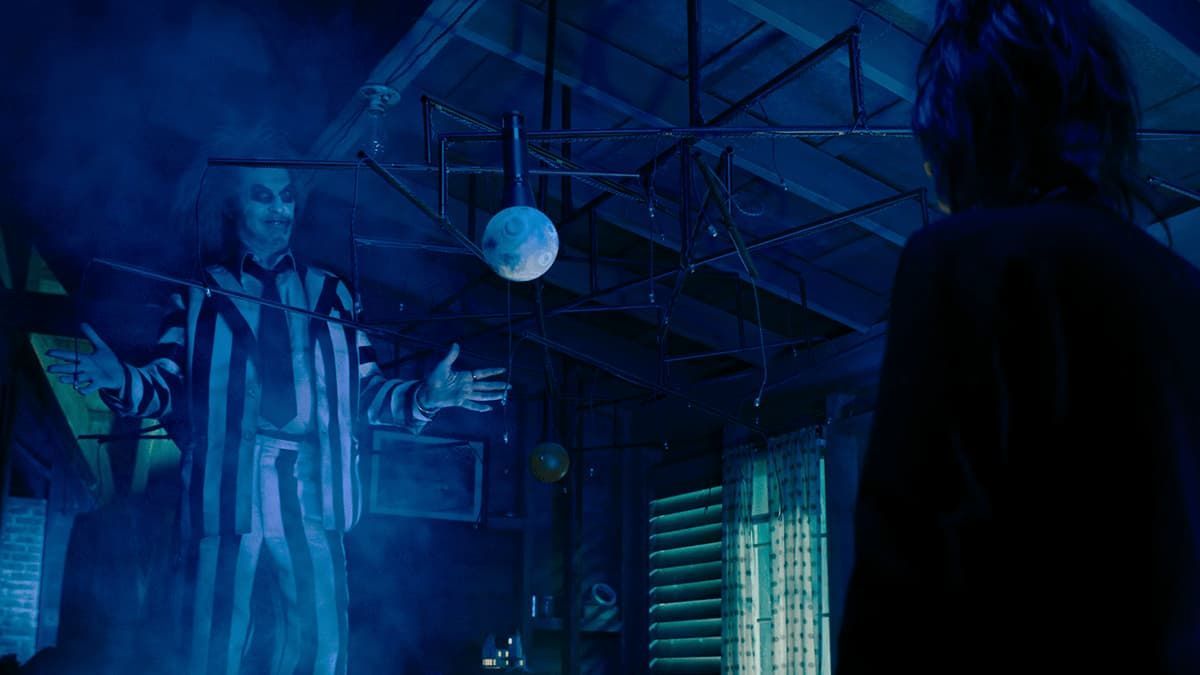 Two figures in a blue-lit industrial room beneath a hanging disco ball, facing each other.