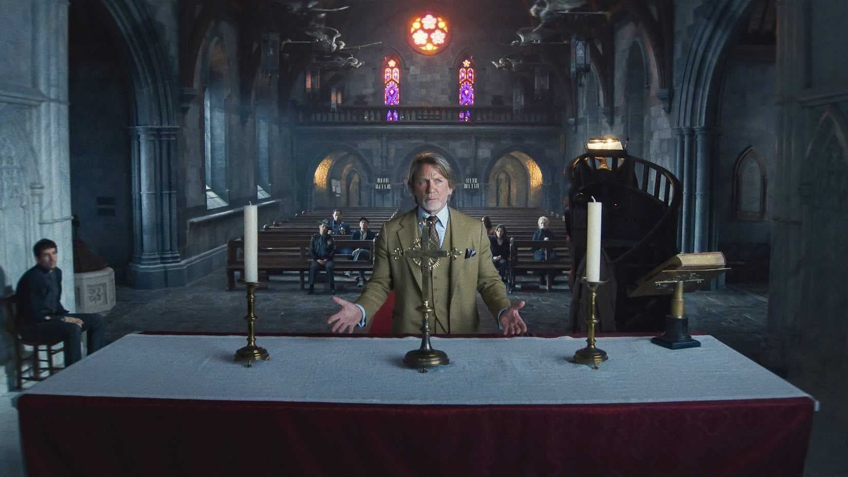 Person in military uniform stands at a long table in a dim cathedral, with stained glass and candelabras behind.