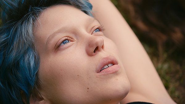Woman with blue hair gazing upwards, lying outdoors.