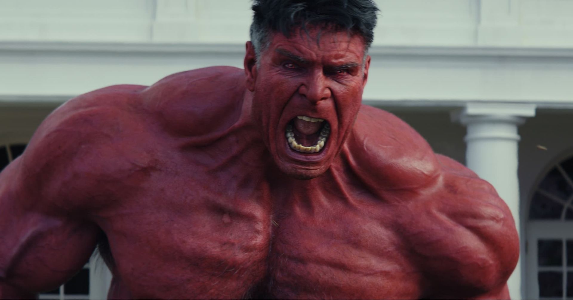 Red Hulk roaring with clenched fists in front of a white building