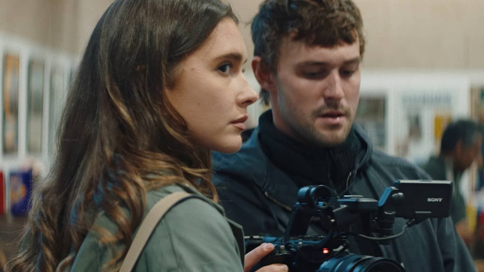 Two people look at a video camera in a store aisle, with shelves blurred in the background.