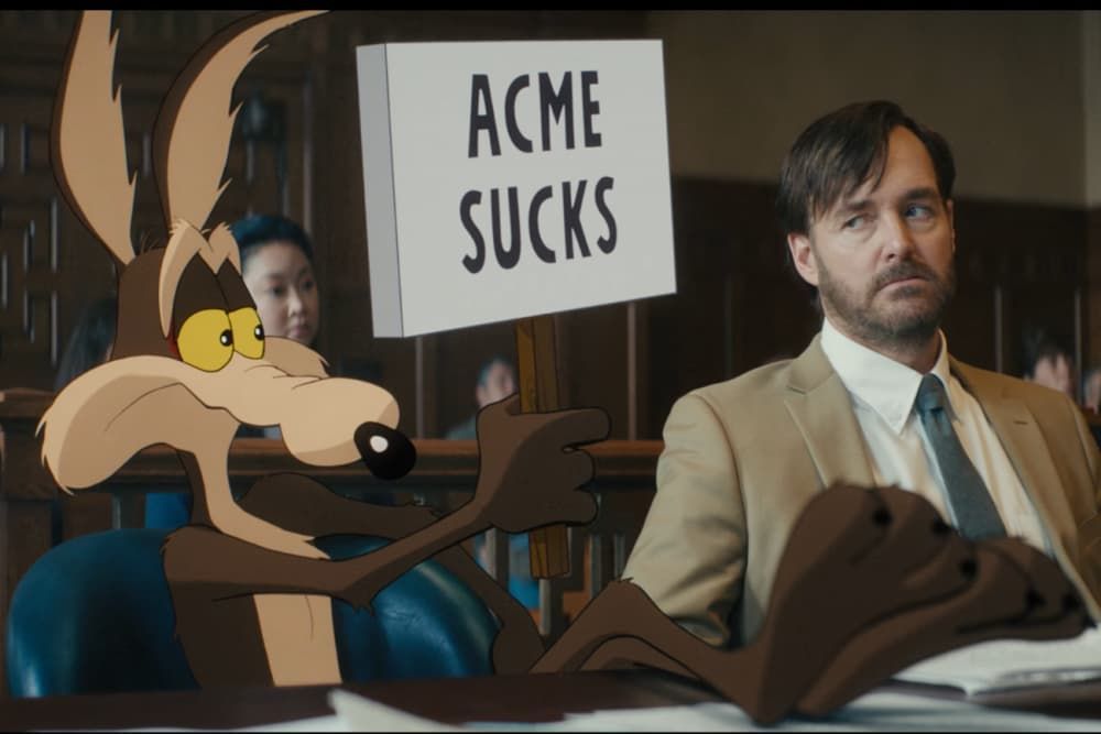 Coyote holds an ACME Sucks sign beside a man in a suit seated at a desk.