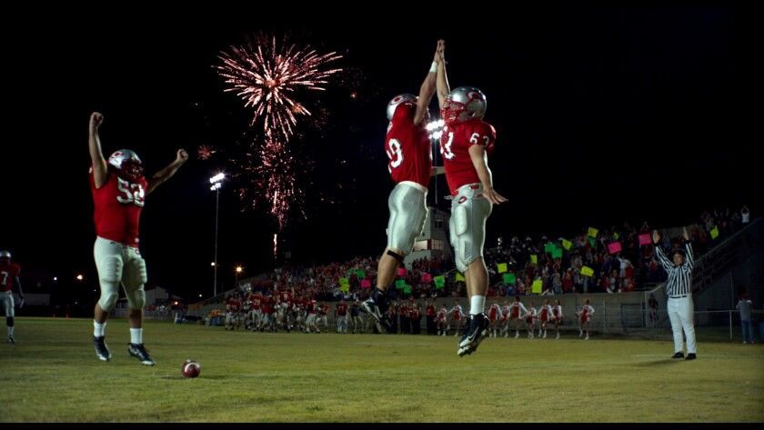 Football players in red uniforms celebrating on the field at night with fireworks and a crowd.