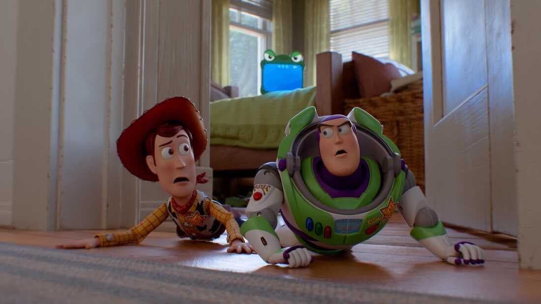 Buzz Lightyear and Woody crawl on a hallway floor, looking startled near a doorway.