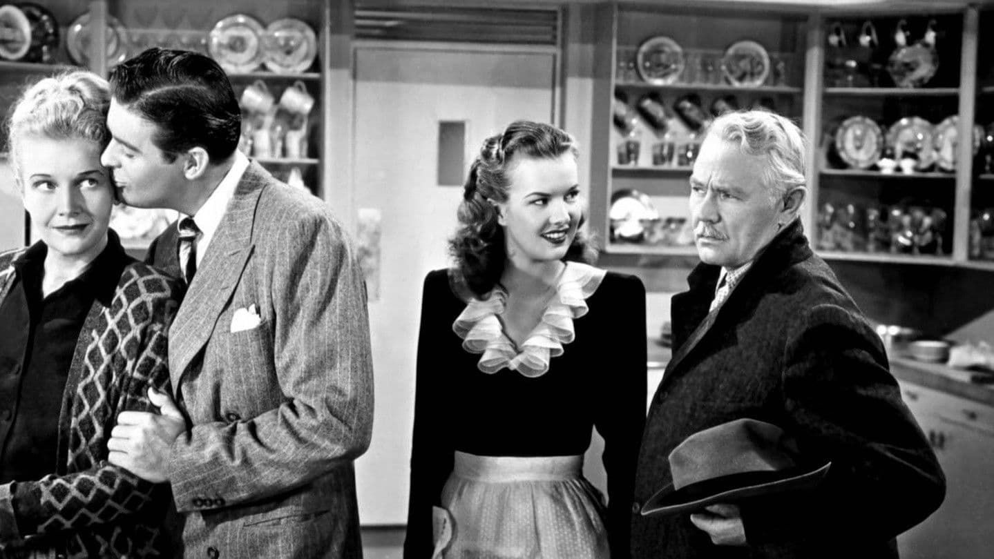 Two men and a woman in a kitchen, with one man whispering to the woman as another man listens.