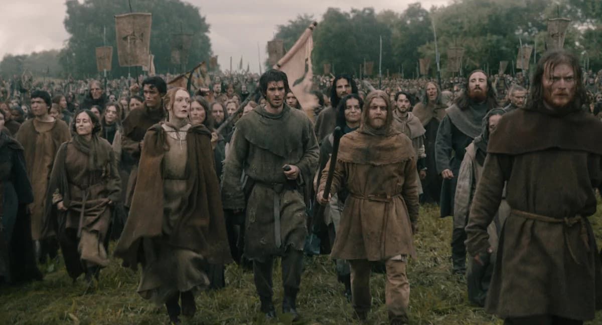 Crowd of weary medieval villagers and soldiers marching through a muddy field under a gray sky
