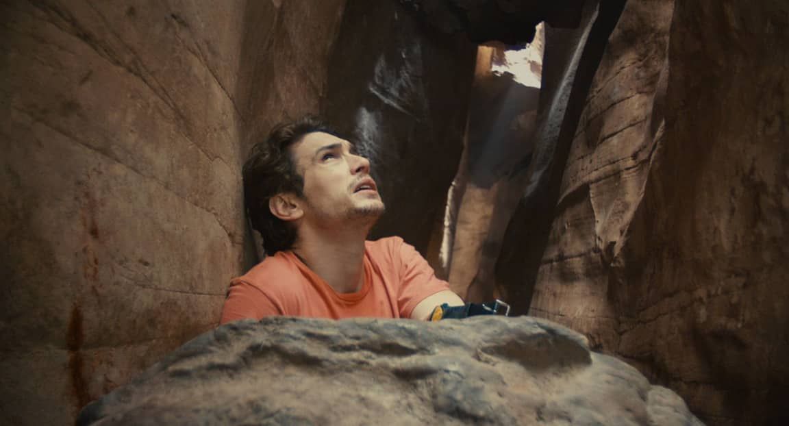 Man trapped in a narrow canyon, looking up in distress. Dark, wet surroundings.