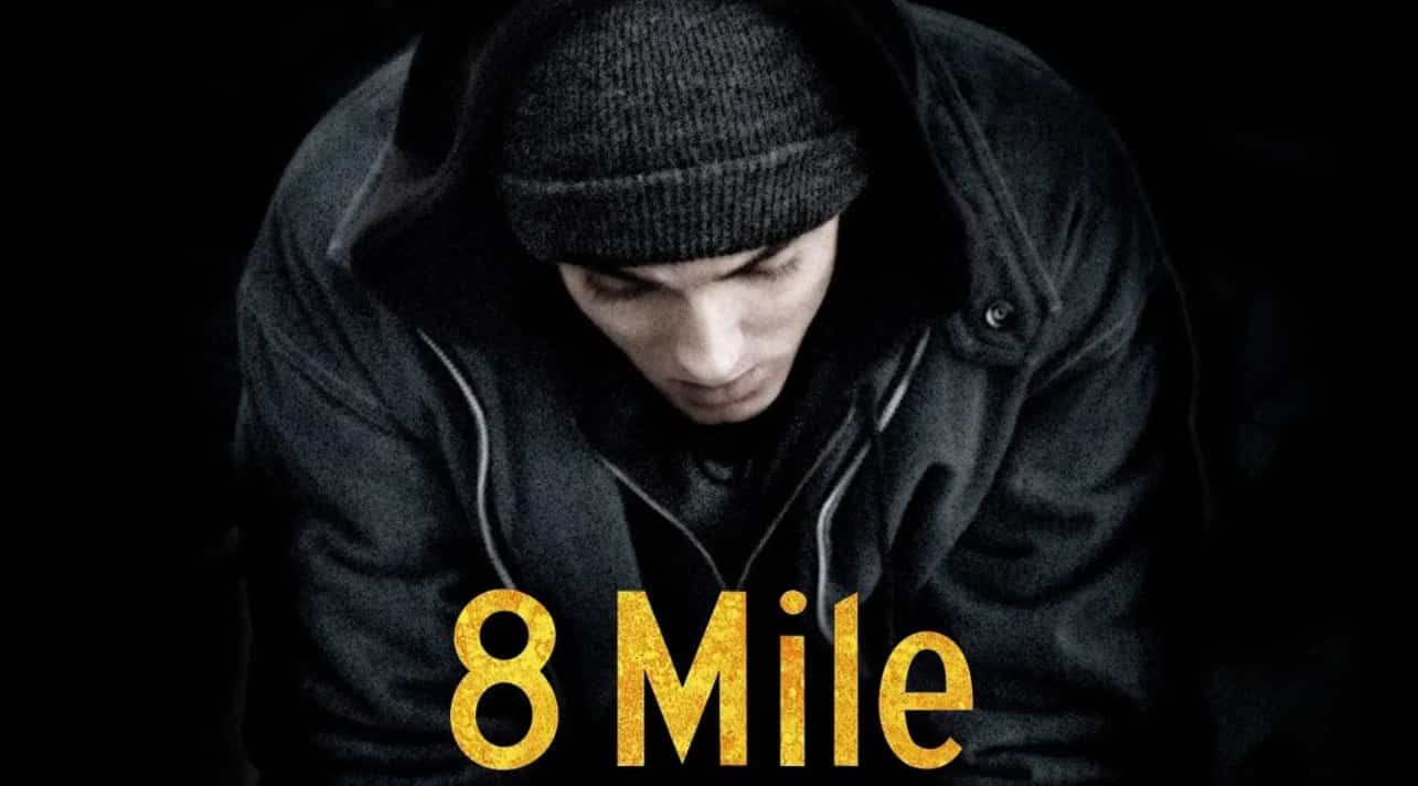 Eminem in a dark hoodie, looking down, against a black backdrop.