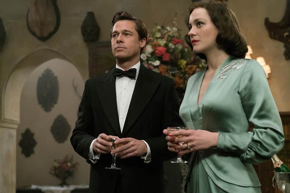 Man in tuxedo and woman in green dress hold champagne glasses, standing together.