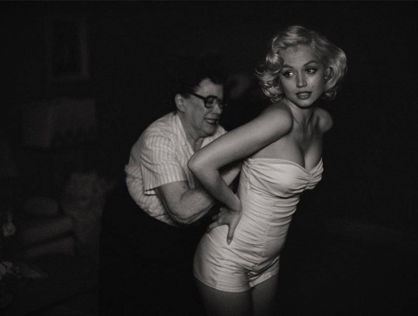 Black and white photo of a man adjusting the back of a woman in a strapless swimsuit.