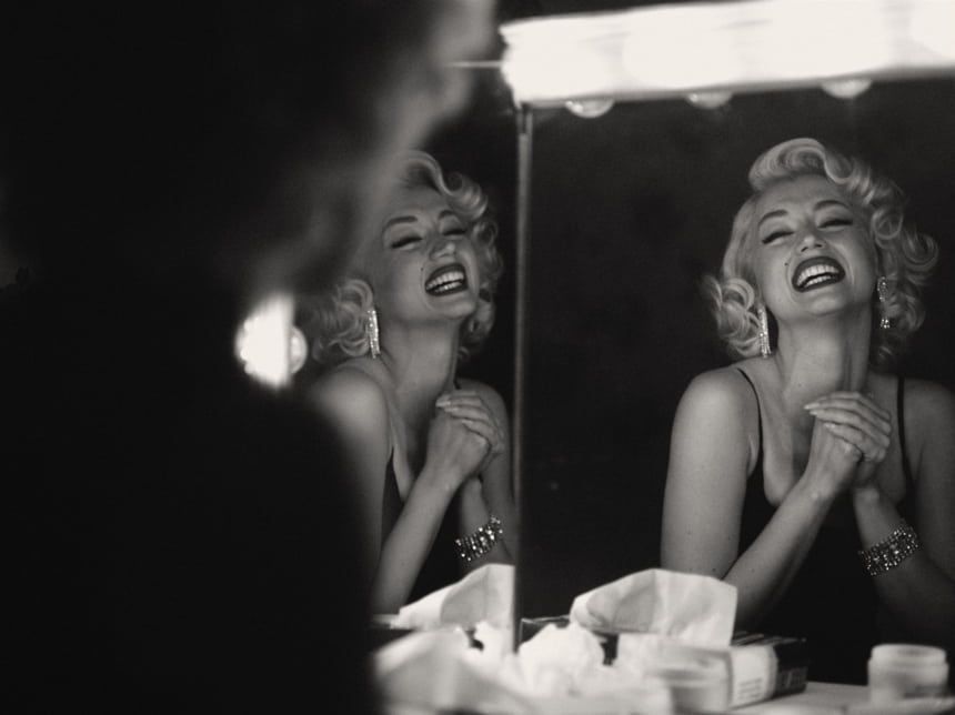 Blonde woman laughing in a mirror, arms clasped, backstage. Black and white photo.
