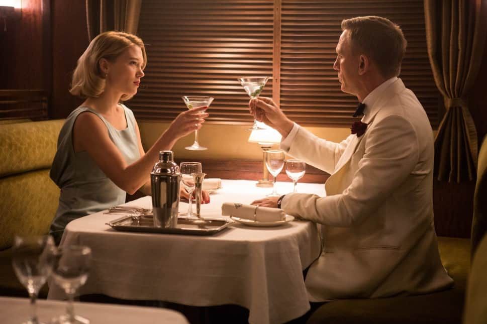 Man and woman in formal attire toasting with cocktails at a restaurant table.