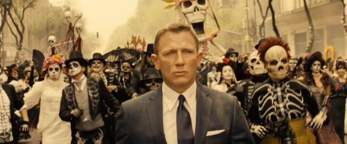 Daniel Craig as James Bond in a Day of the Dead parade, wearing a suit, with a serious expression.