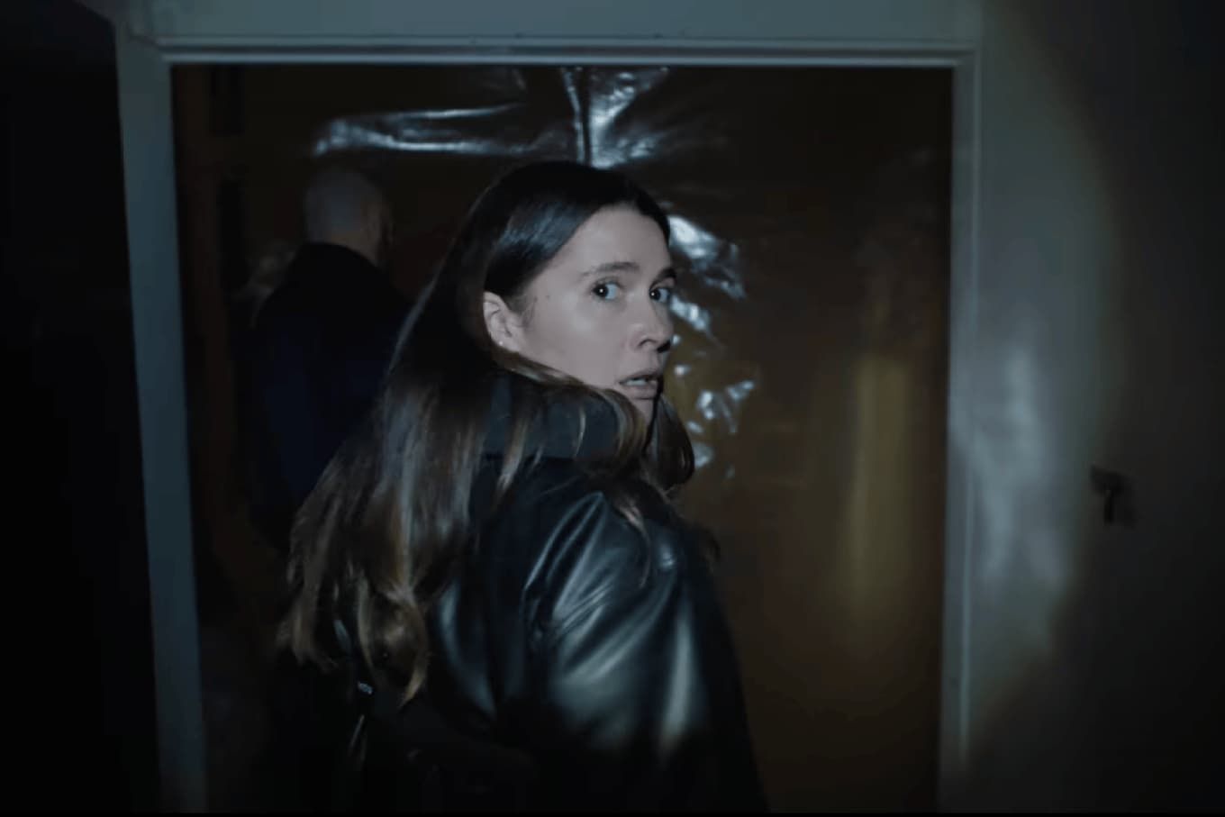 Woman in a black leather jacket looking back in a dark doorway.