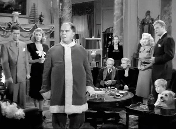 Black-and-white film scene with a man in a Santa suit standing in a room with several onlookers.