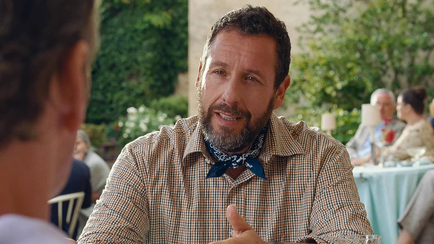 Man at an outdoor table in a patterned shirt and bow tie, speaking to someone off-camera.
