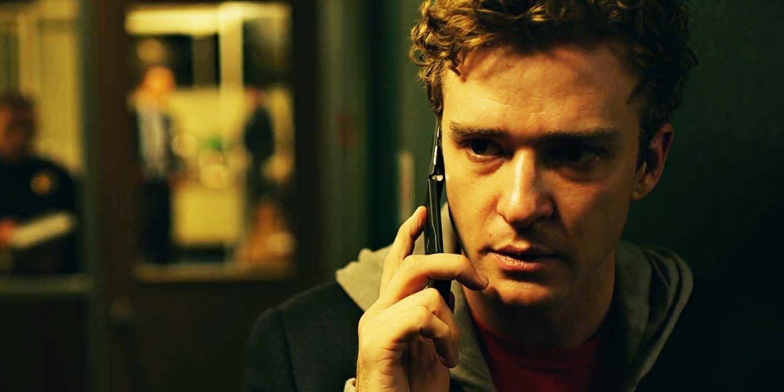 Man indoors, holding a phone to his ear in a dimly lit room, with a serious expression